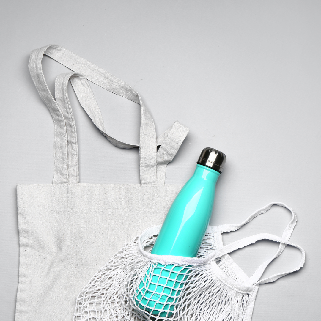 The image shows a light blue water bottle in a white mesh bag, which is inside a white tote bag, all on a light gray background.