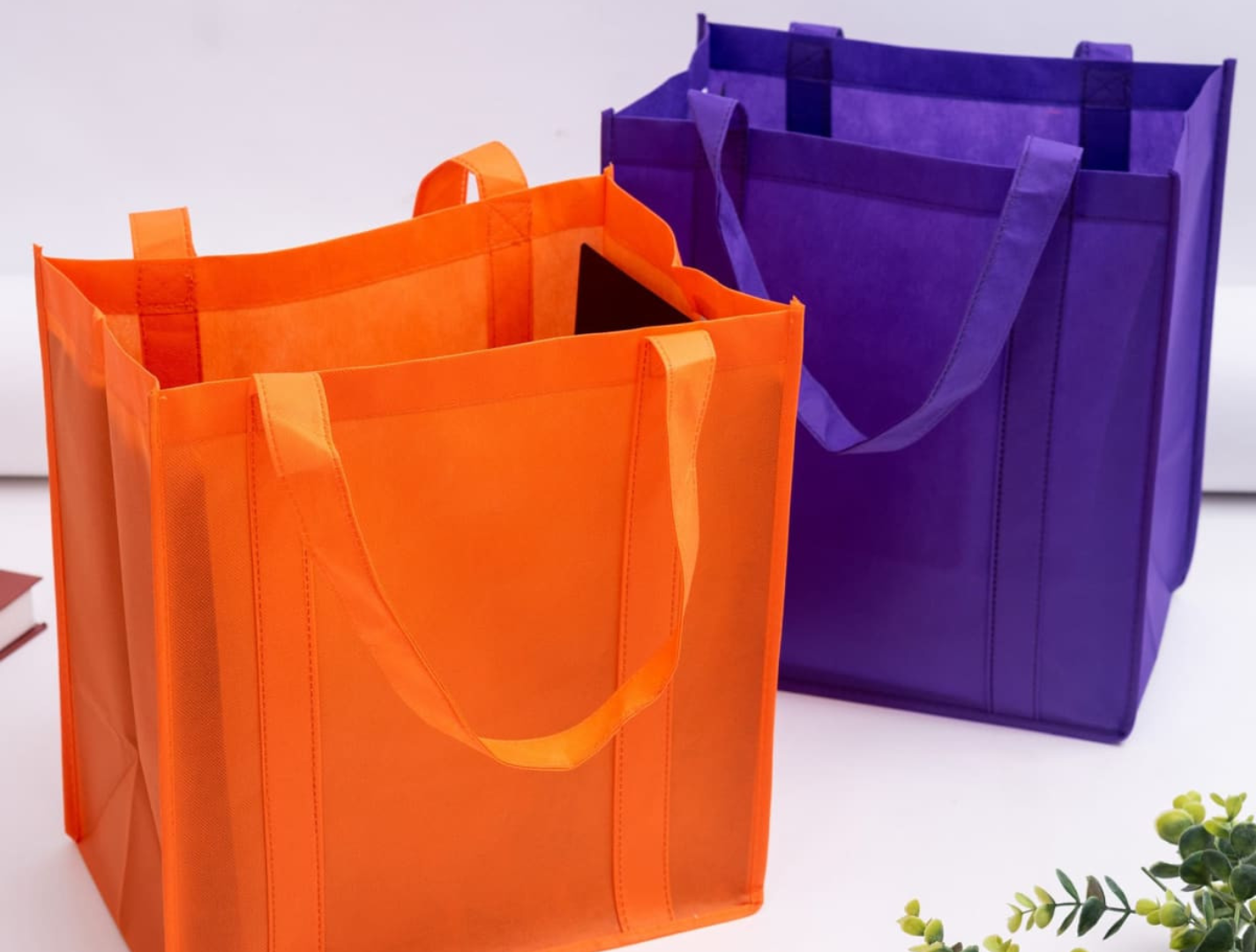 Two reusable shopping bags in vibrant orange and purple, featuring a sturdy handles and structured design.